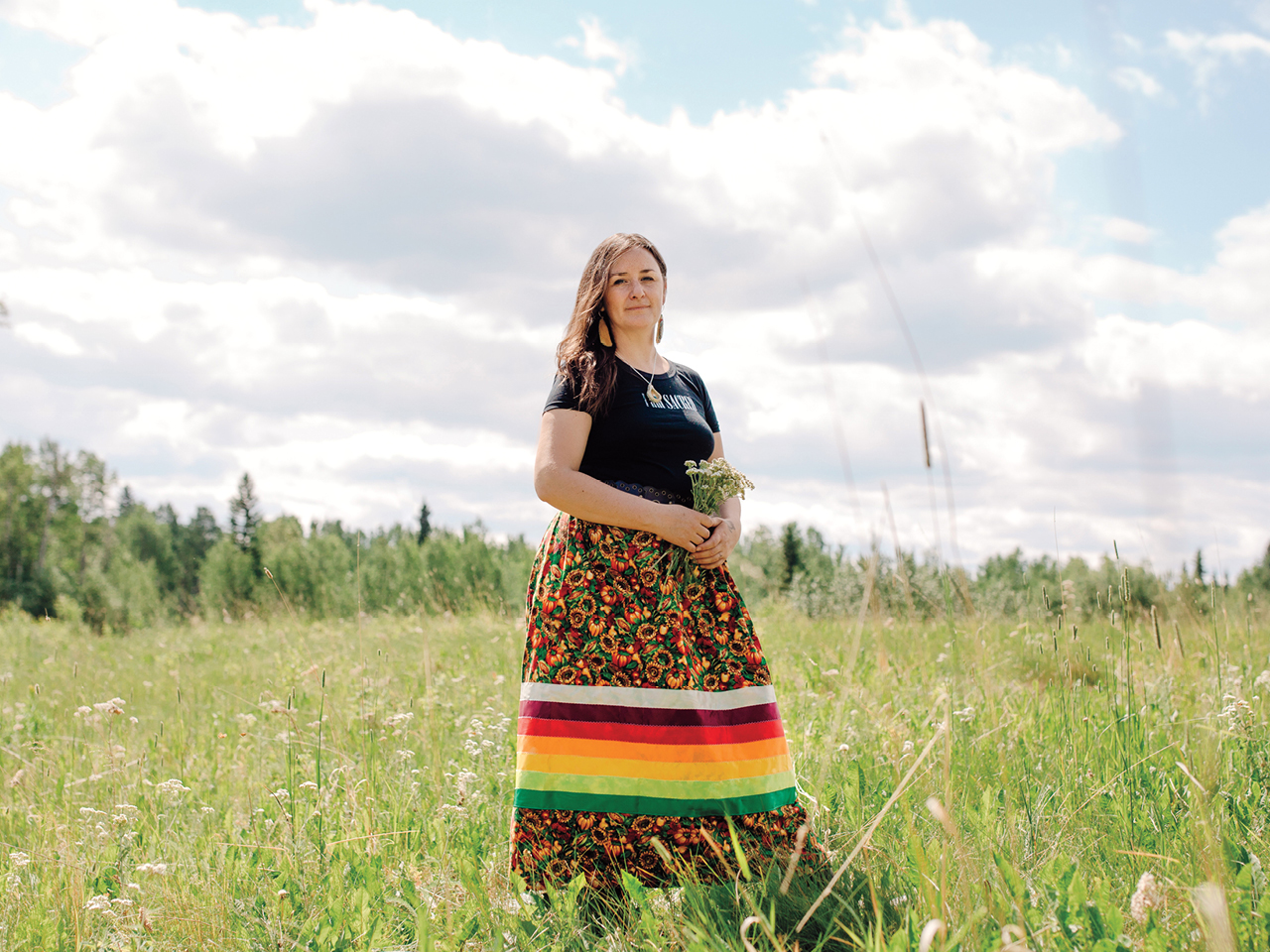 Tiffany Traverse stands in a field, she is holding a small bouquet of flowers