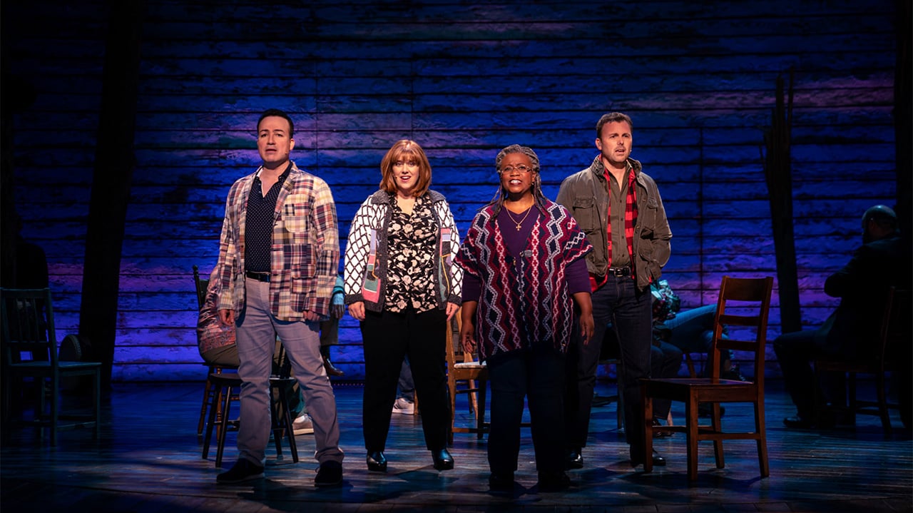 Four cast members of the filmed stage production of COme From away stand on stage, singing