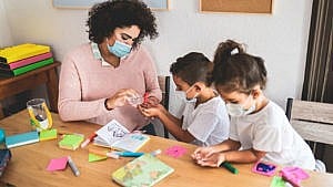 A daycare teacher wearing a mask squeezes hand sanitizers into the hands of two masked students for a piece on the various child care promises by the federal parties in the Canada election 2021