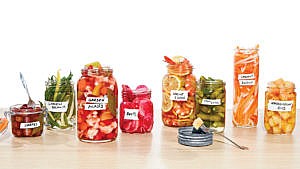Eight jars of various pickle recipes sit next to one another on a table.