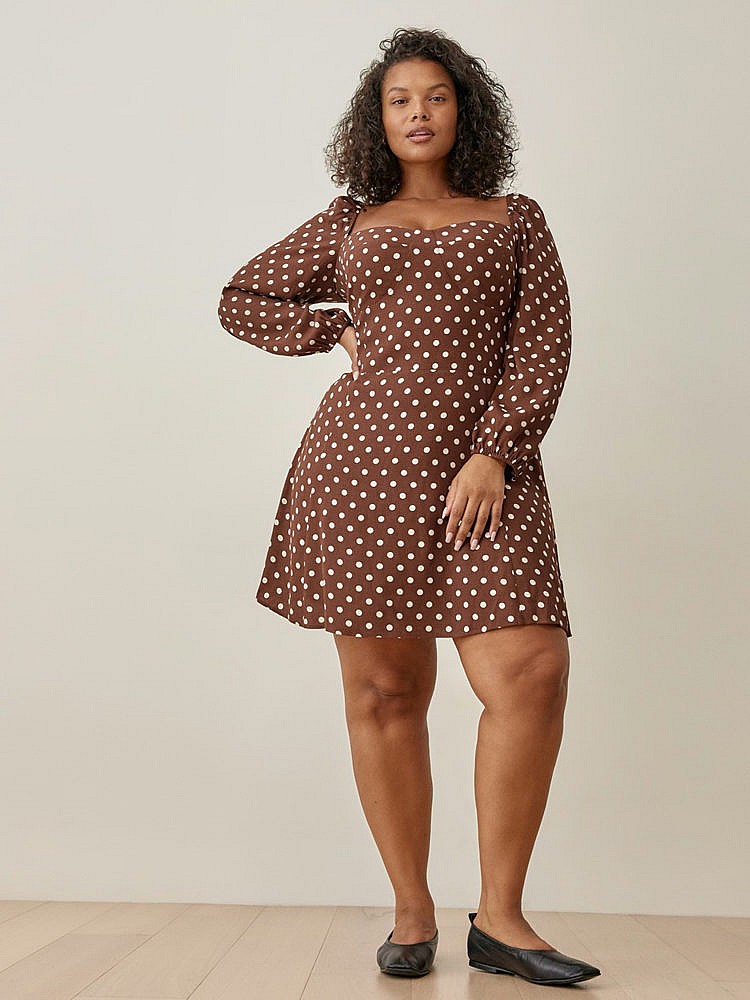 A model wearing reformation\'s brown with white polka dots, long sleeves and a sweetheart neckline dress with black flats