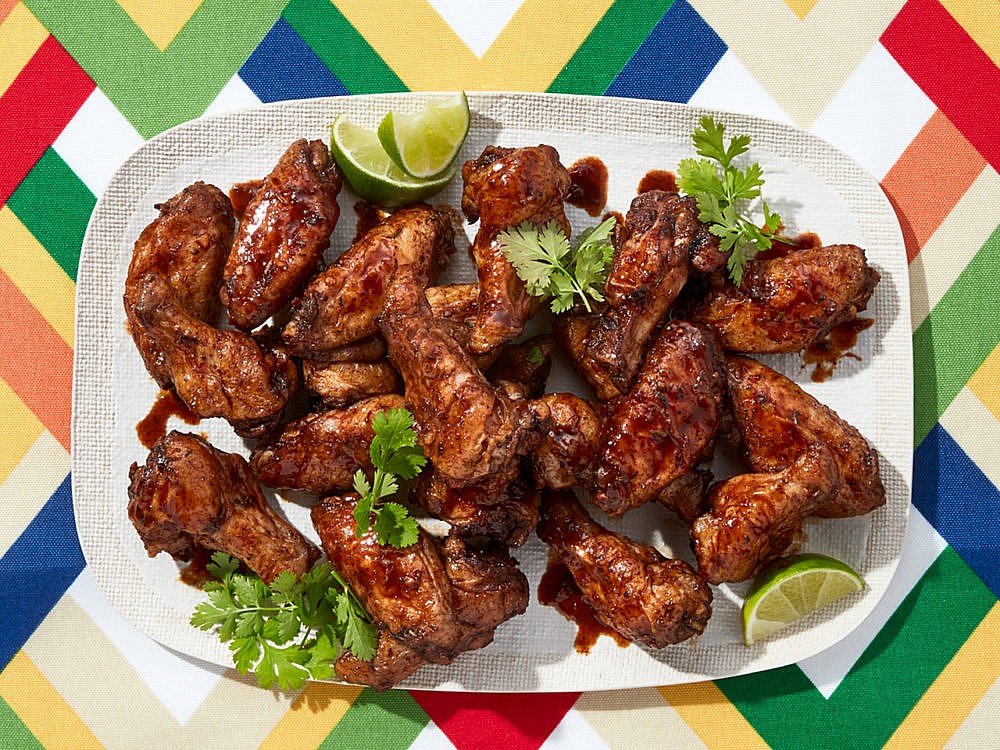 A white plate of jerk chicken wings sitting on a colourful tablecloth.