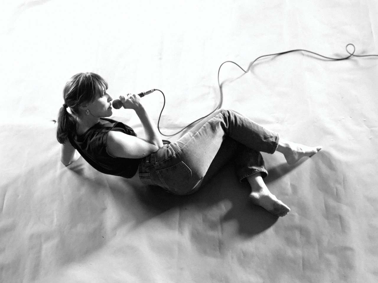 A black and white photo of Leslie Feist, holding a microphone, lying down on stage