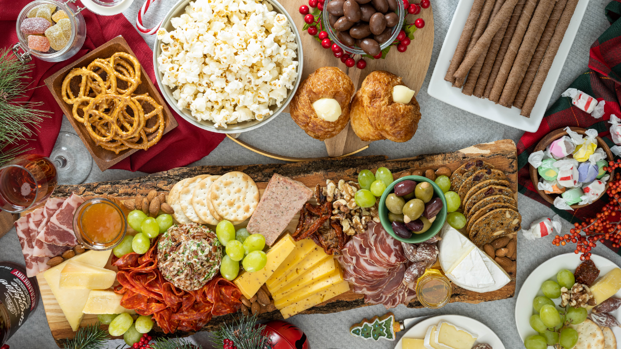 A bowl of popcorn and a bowl of chocolate-covered almonds sit next to a charcuterie board with meats and cheeses on it.