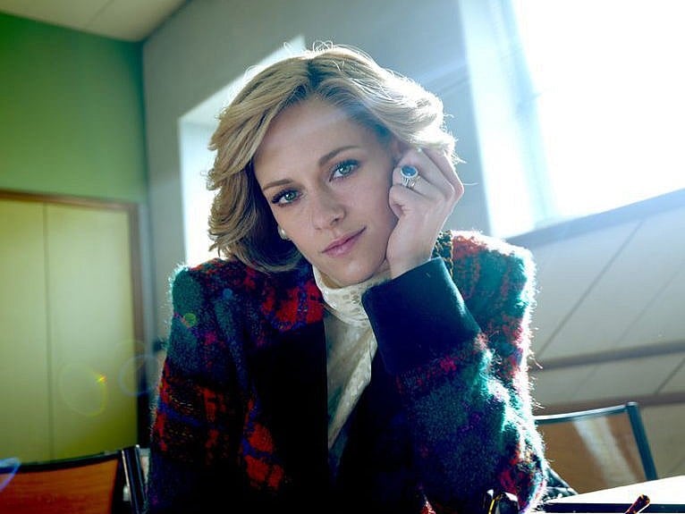 A still from the movie Diana, with Kristen Stewart as Princess Diana, she wears a colourful tweed jacket and leans her ringed hand against her head