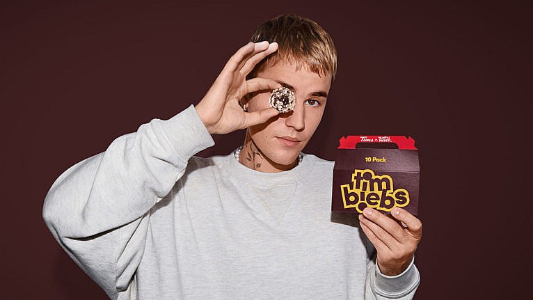 A box of Timbits with the logo Timbiebs sits on a table with three crumb coated timbits next to it.
