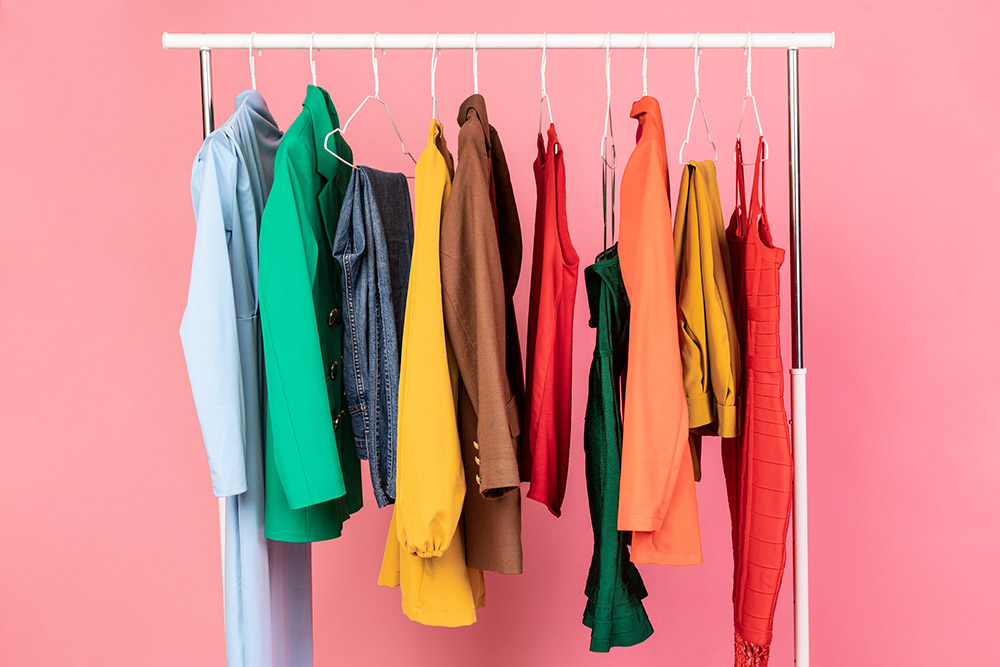 Clothing Rail With Clothes Over Pink Background In Studio. Colorful Outfits Hanging On Hangers.