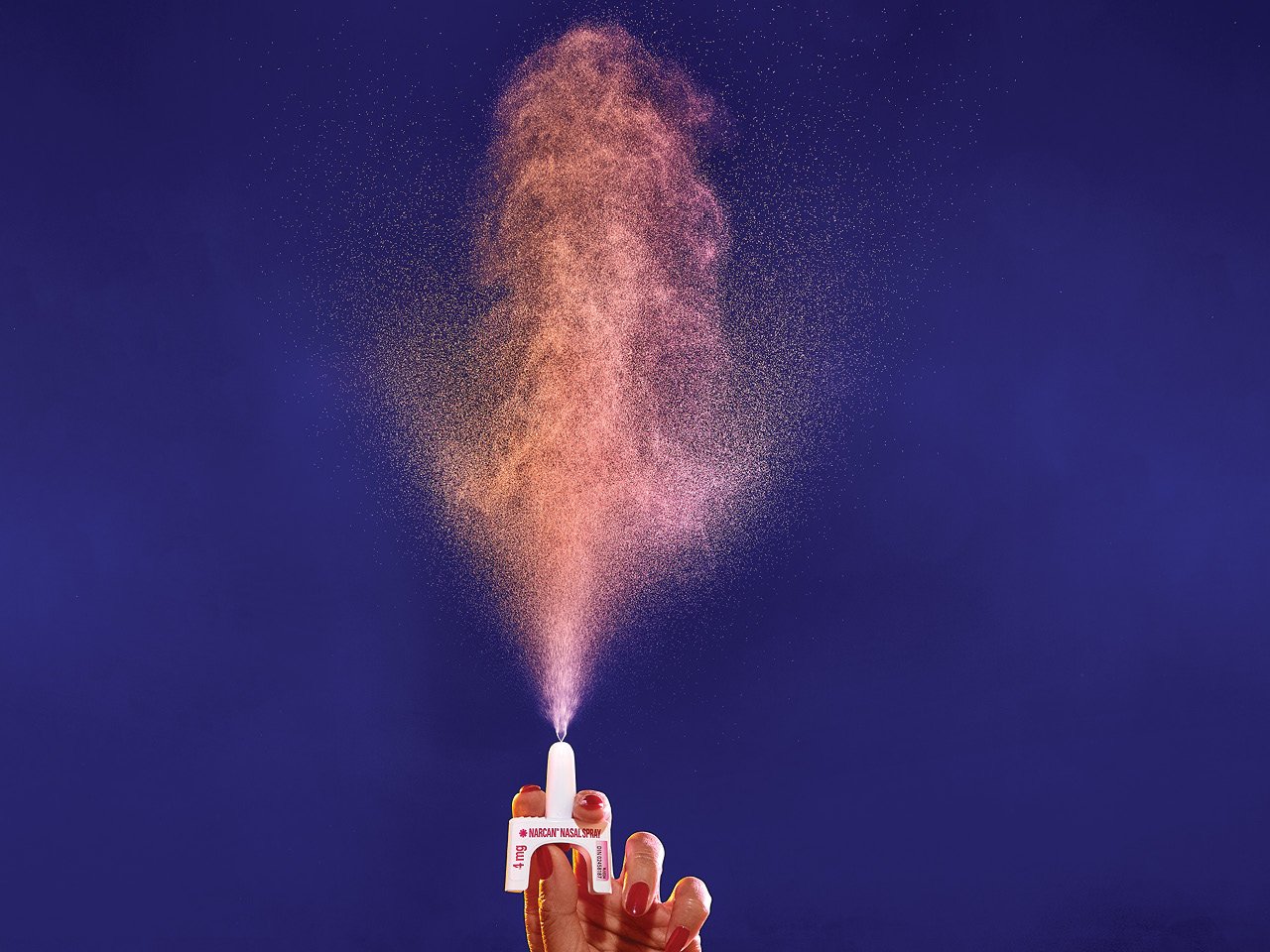 A woman's hands spraying naloxone into the air against a dark blue background.