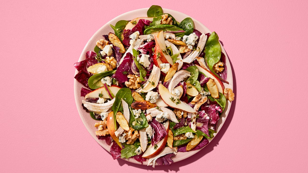 Lettuce with pears, nuts and shredded chicken on a pink plate.