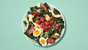 A salad of kale with tomatoes, eggs, avocado on a green plate on a green table.