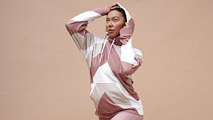 A model against a pink background wearing a pink and cream striped Lesley Hampton workout set.
