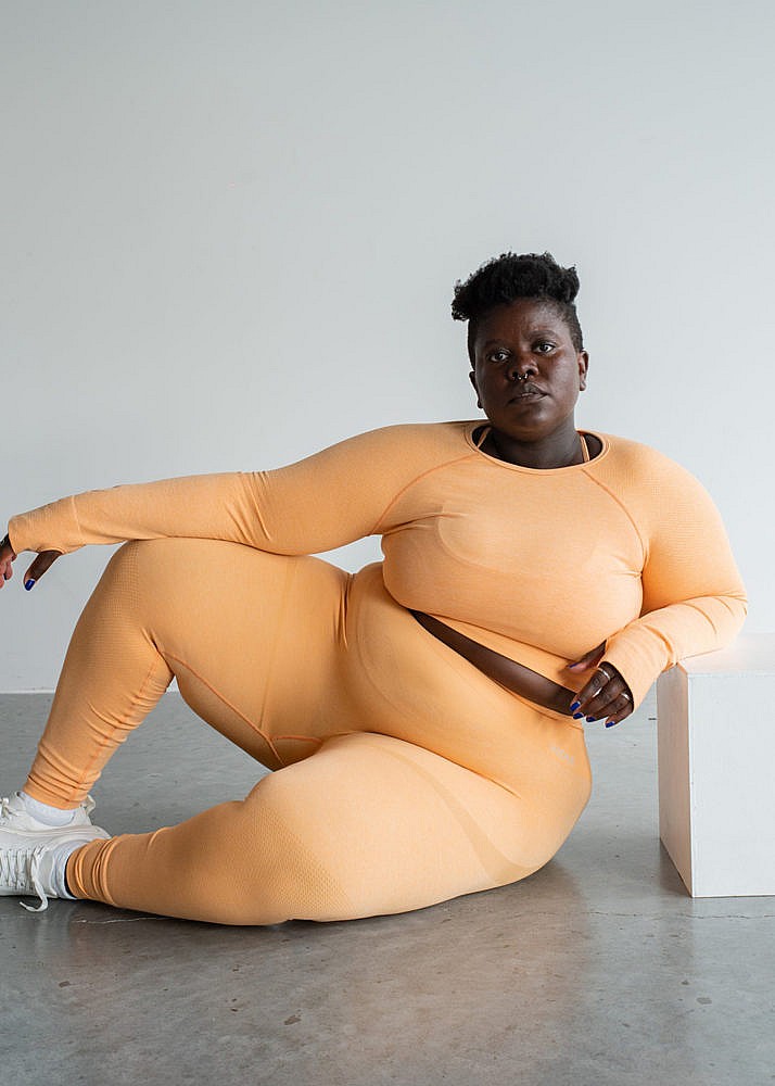 A model wearing sitting on the floor wearing an orange workout set from Vitae Apparel.