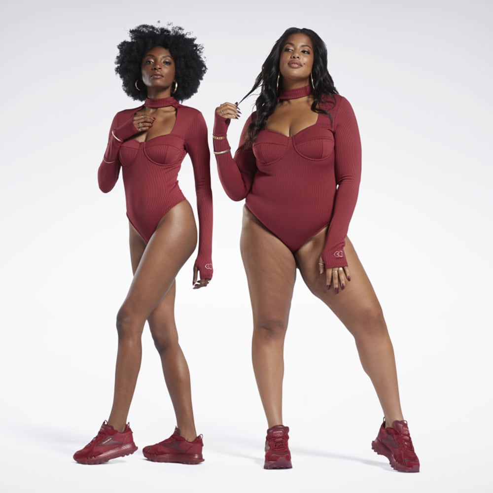 Two models standing against a white background wearing red cut-out workout bodysuits by Reebok x Cardi B.