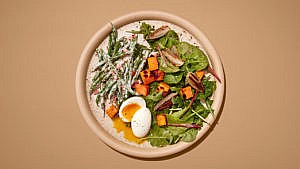 Salad with beans, leafy greens, soft boiled egge and sweet potato in a brown dish on a brown table.
