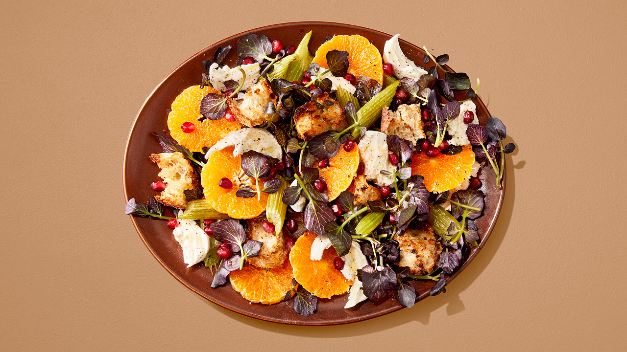 Salad with clementines, pomegranate seeds and watercress in a brown bowl on a brown table.