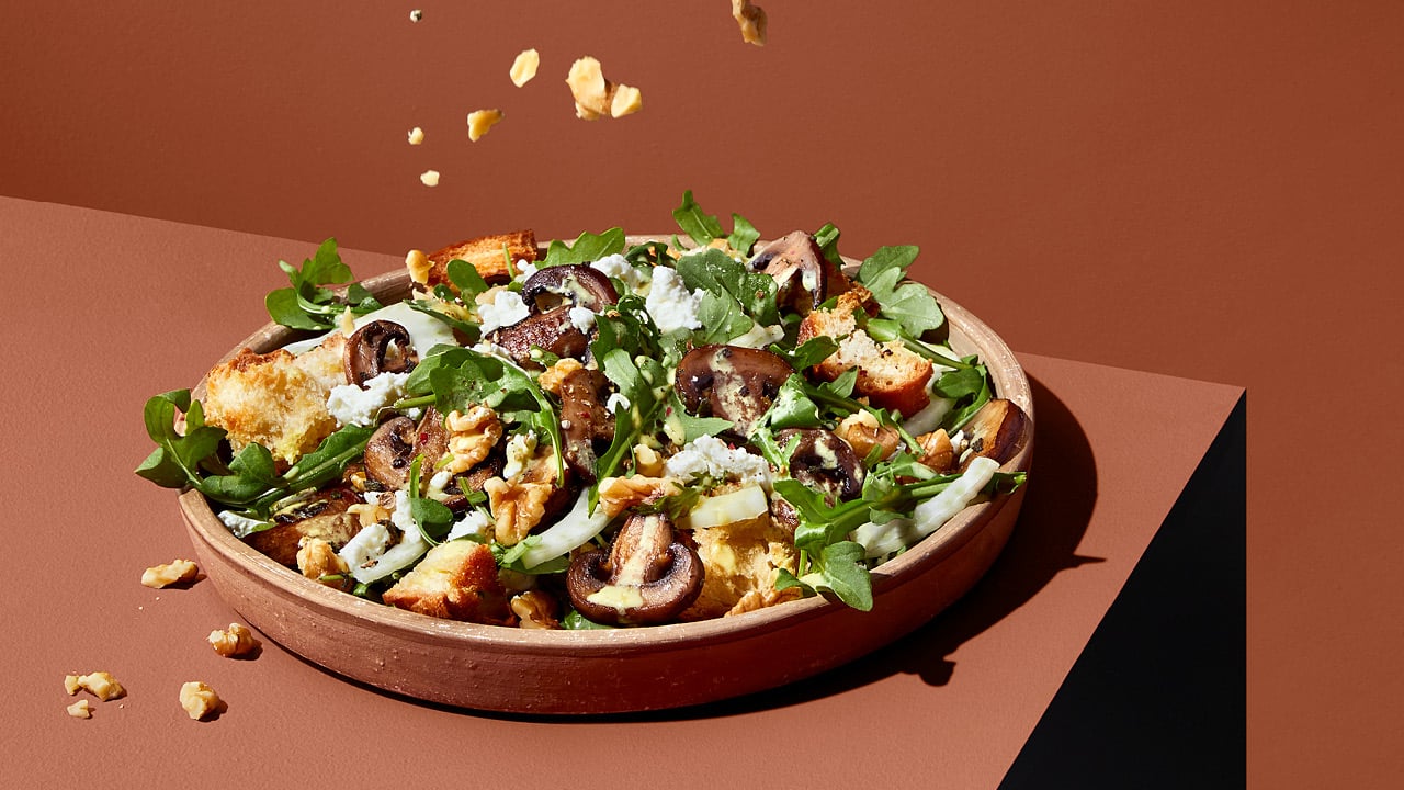 Salad with mushrooms, cheese and nuts in a brown bowl on a brown table.