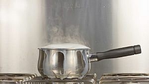 A steel saucepan of milk boils over on a gas stove