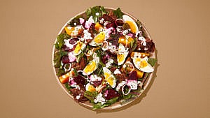 Salad with eggs, beets, and croutons on a brown plate on a brown table.
