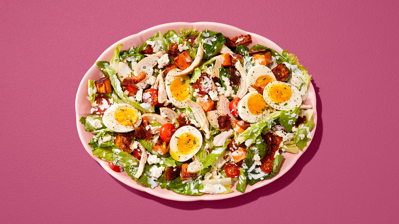Cobb salad with sliced ​​soft-boiled eggs, tomatoes and chicken in a pink bowl on a pink table.