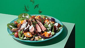 Salad with steak and potatoes in a green bowl on on a green table.
