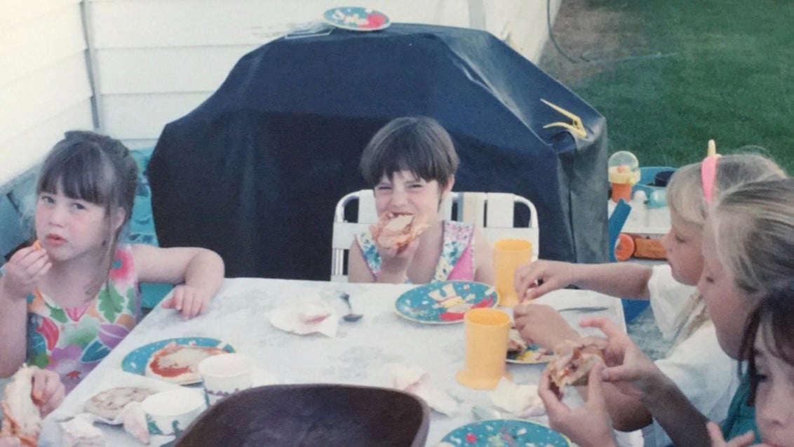 A childhood photo of Megan eating a sandwich outdoors.