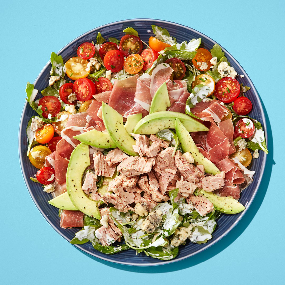 A salad with avocado, tuna, tomatoes on a blue plate on a blue table.