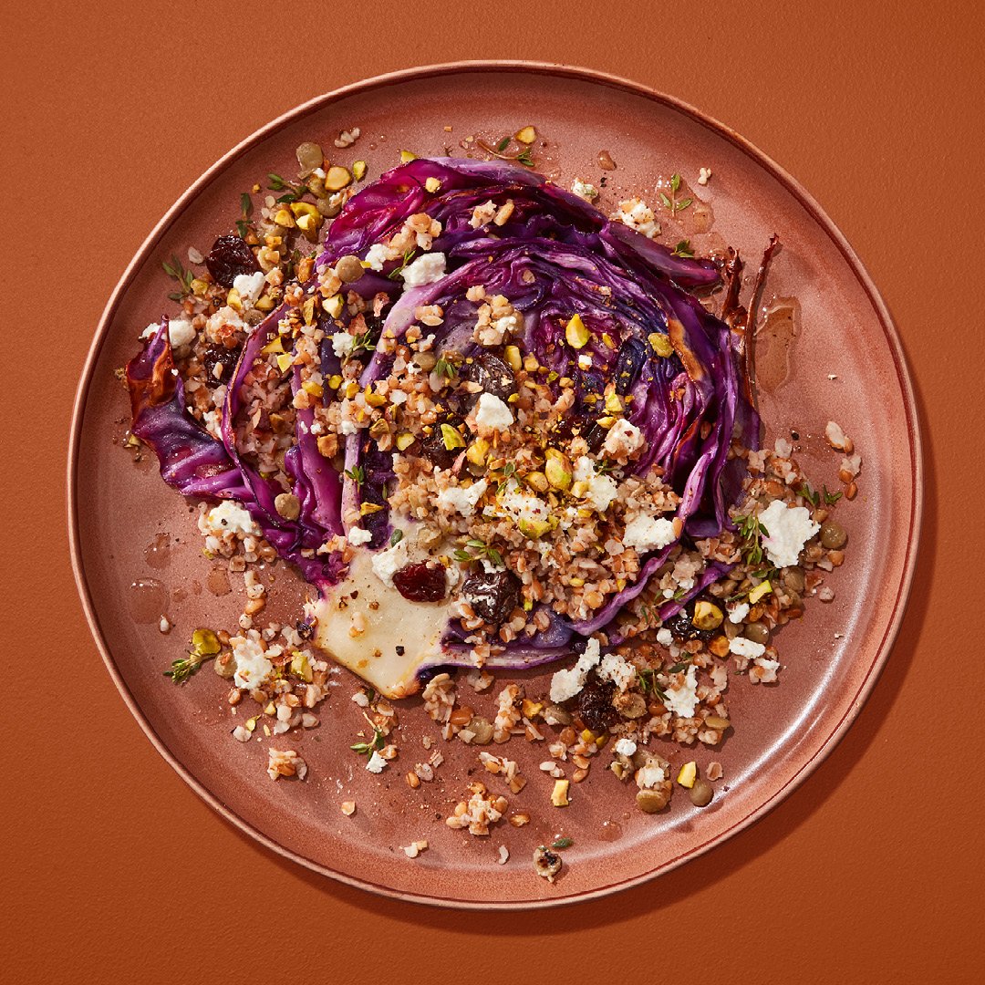 Slice of red cabbage topped with lentils, dried cherries and pistachios on a brown plate on a brown table.