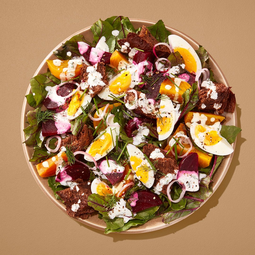 Salad with eggs, beets, and croutons on a brown plate on a brown table.