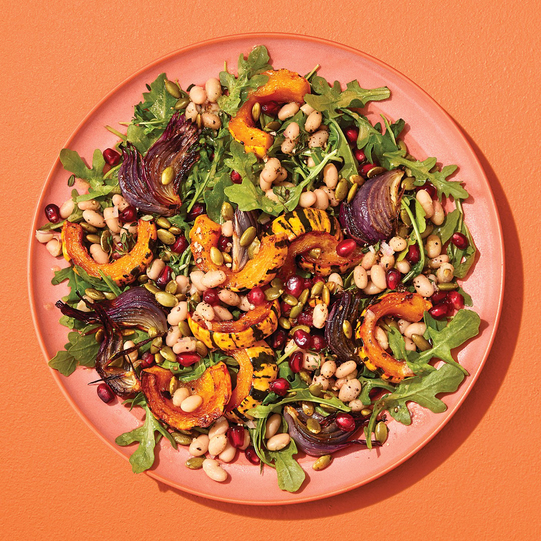 Colourful salad with beans, arugula and squash on an orange plant on an orange table.