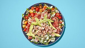 A salad with avocado, tuna, tomatoes on a blue plate on a blue table.