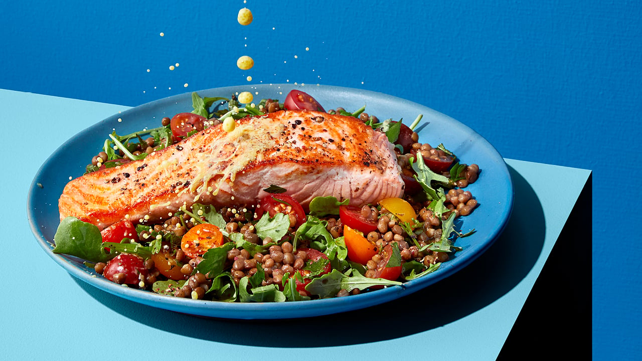 A salad with salmon, tomatoes and arugula on a blue plate on a blue table.