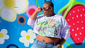 London Blackwood wears a secondhand crop top in front of a brightly-painted wall.