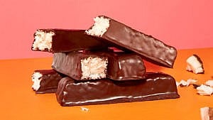 A stack of chocolate-covered coconut bars on a pink background