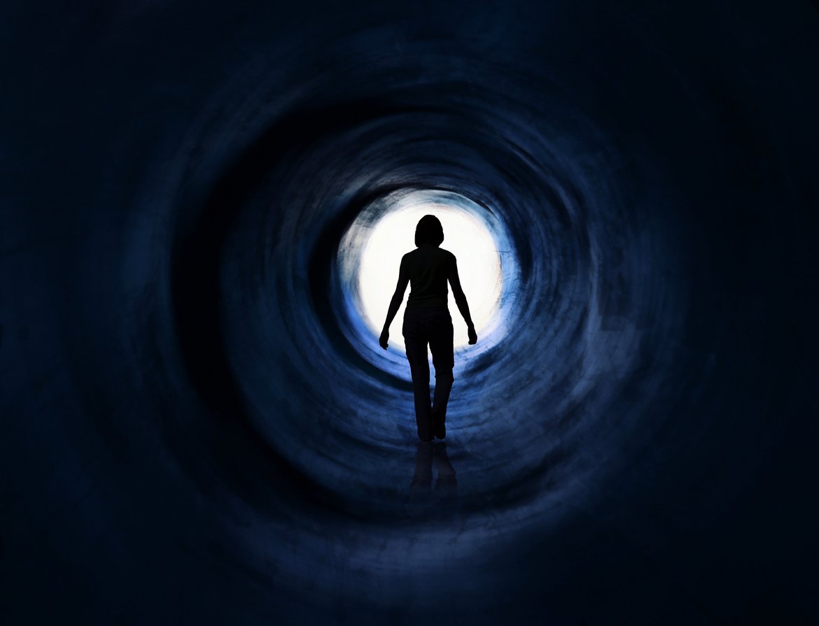 A woman in a dark tunnel walking towards the light