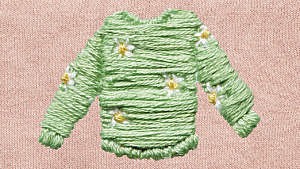 A green embroidered sweater with a daisy pattern on a pink cloth background