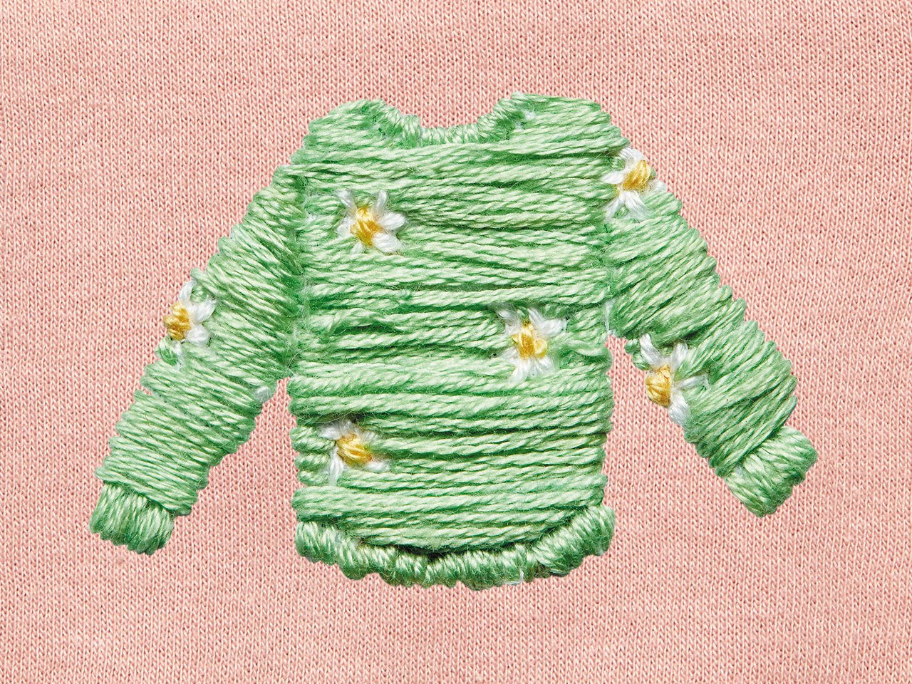 A green embroidered sweater with a daisy pattern on a pink cloth background