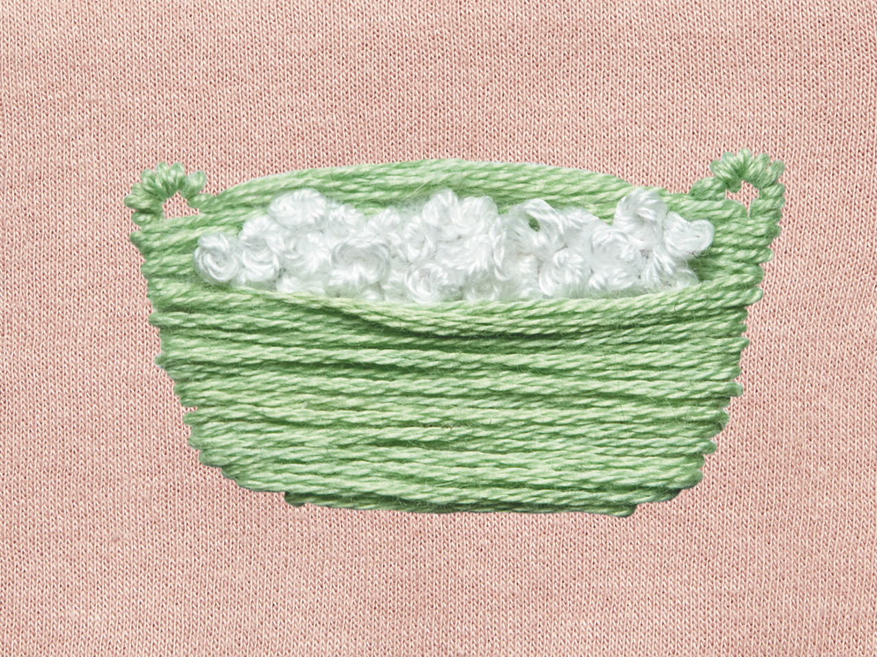 Green laundry basket embroidered with white foam on a pink cloth background