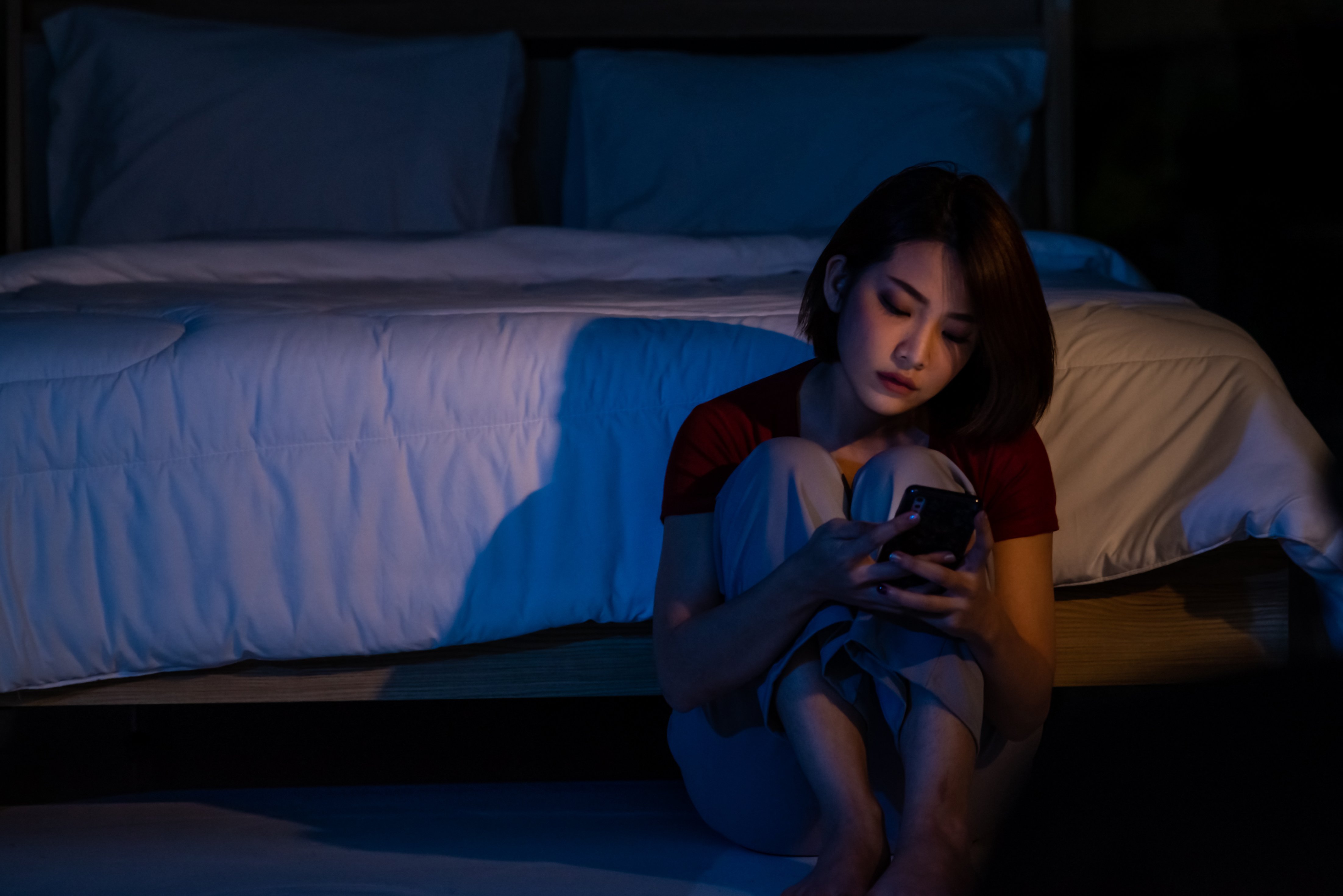 Nighttime scene of Asian woman sitting on the floor looking at her phone