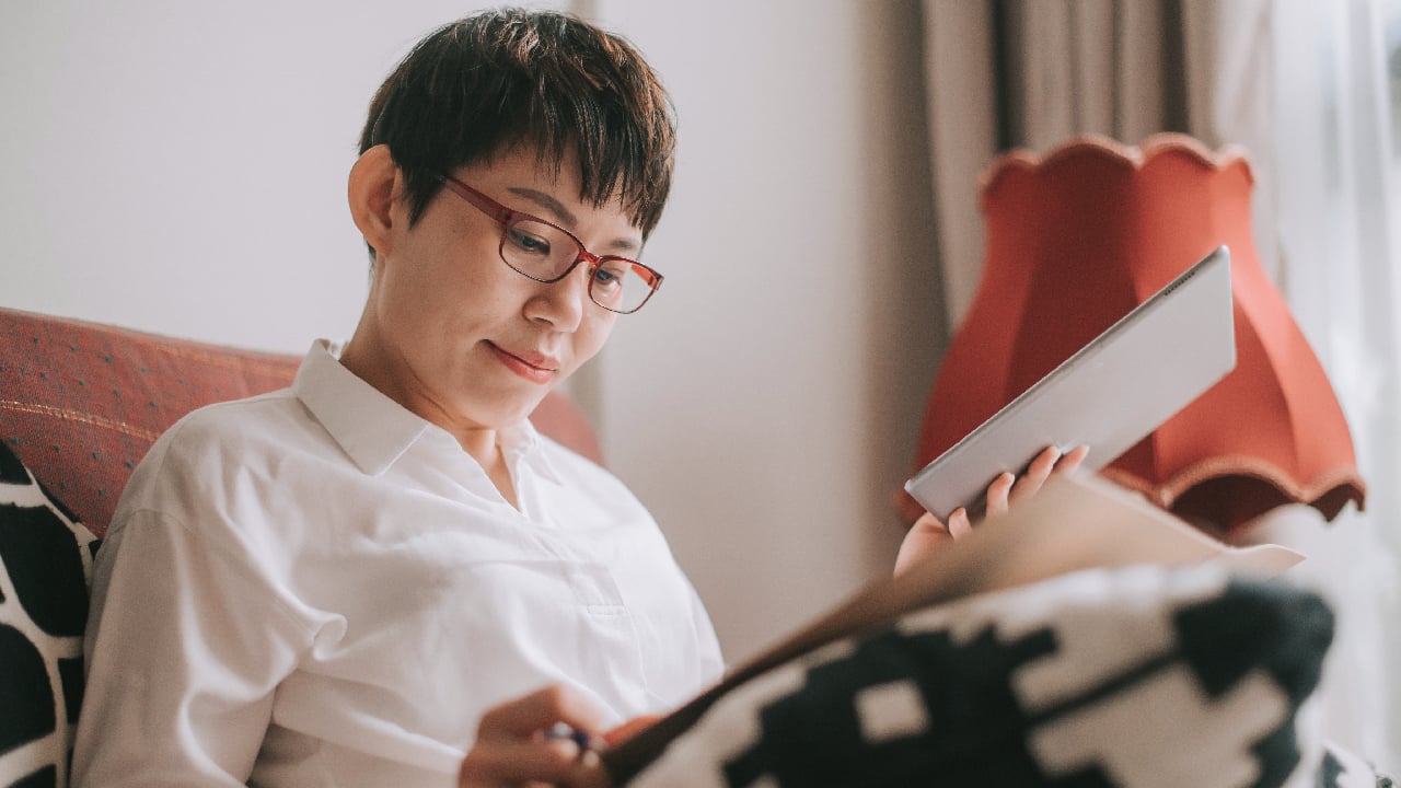 A woman sitting on a couch reading with reading glasses on.