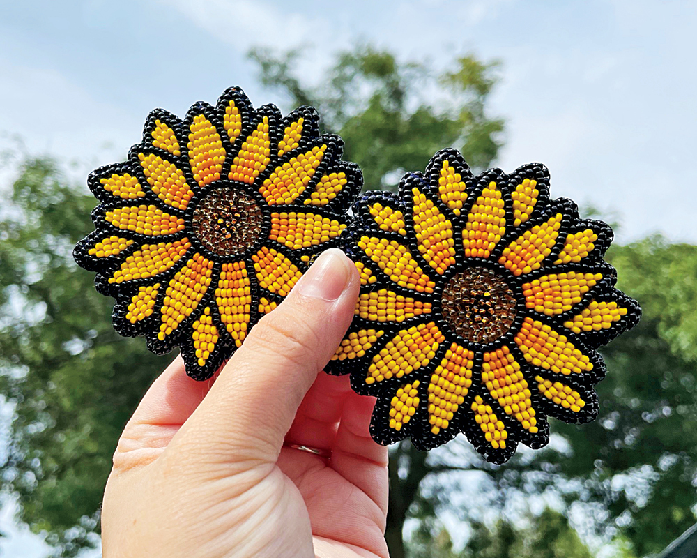 A hand holds up a pair of beaded sunflowers against an outdoor backdrop