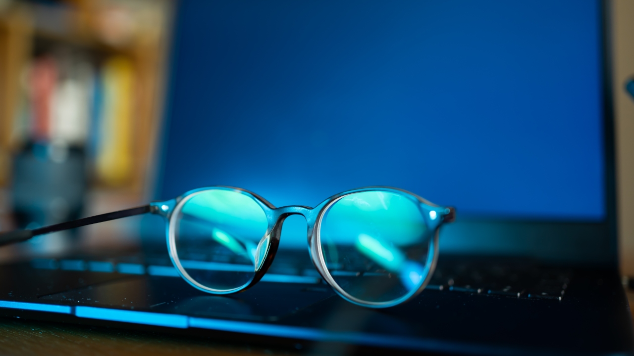A pair of blue light glasses on the keyboard of a laptop.