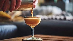 A person pouring an espresso martini out of a cocktail shaker and into a glass