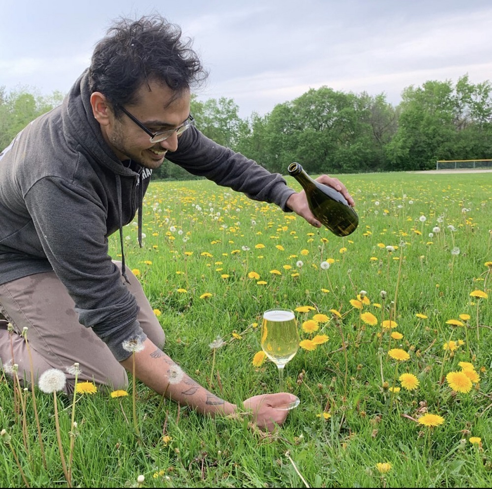Forager Tariq Ahmed pouring cider into a glass on a field of dandelion flowers for a feature on foraging for spring foods