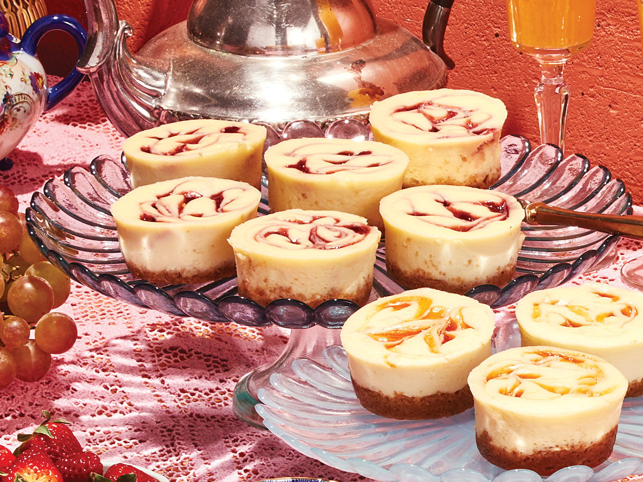 Several jam swirl mini cheesecakes on a serving dish laid on top of a pink lace tablecloth
