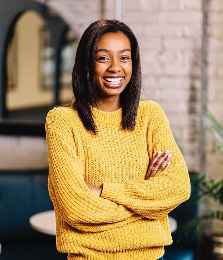 A photo of a woman, Khadijah Plummer, wearing a yellow sweater and smiling for a feature on working women during the pandemic