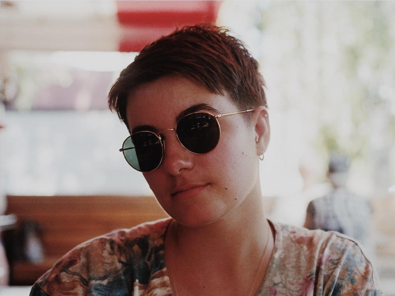 A photo of a woman with short brown hard and gold-rimmed sunglasses