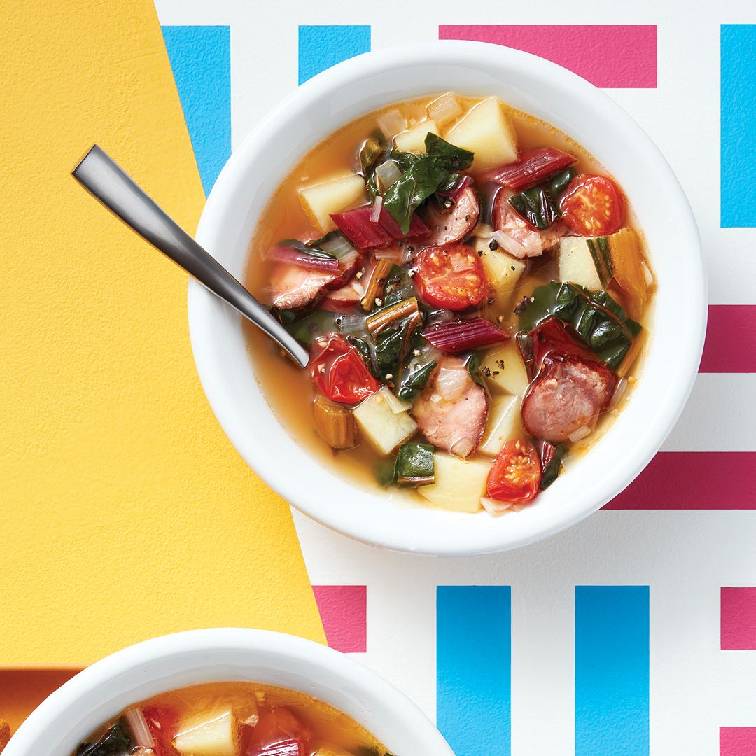 Rainbow chard, tomatoes, sausage, and potatoes in white soup bowl and silver spoon. 