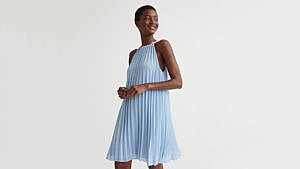 A model wearing a short blue pleated H&M dress for a round-up of summer wedding guest dresses.