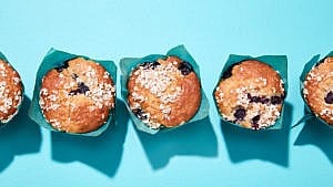 Three blueberry muffins with blue wrapper on blue background.
