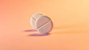 two pink pills against a soft orange background